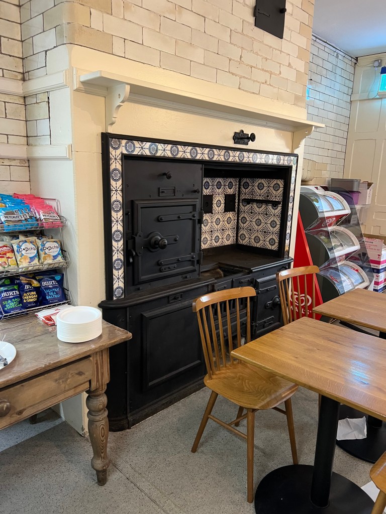 The cafe with wooden tables in front of a large black range stove with blue and white tiles. 