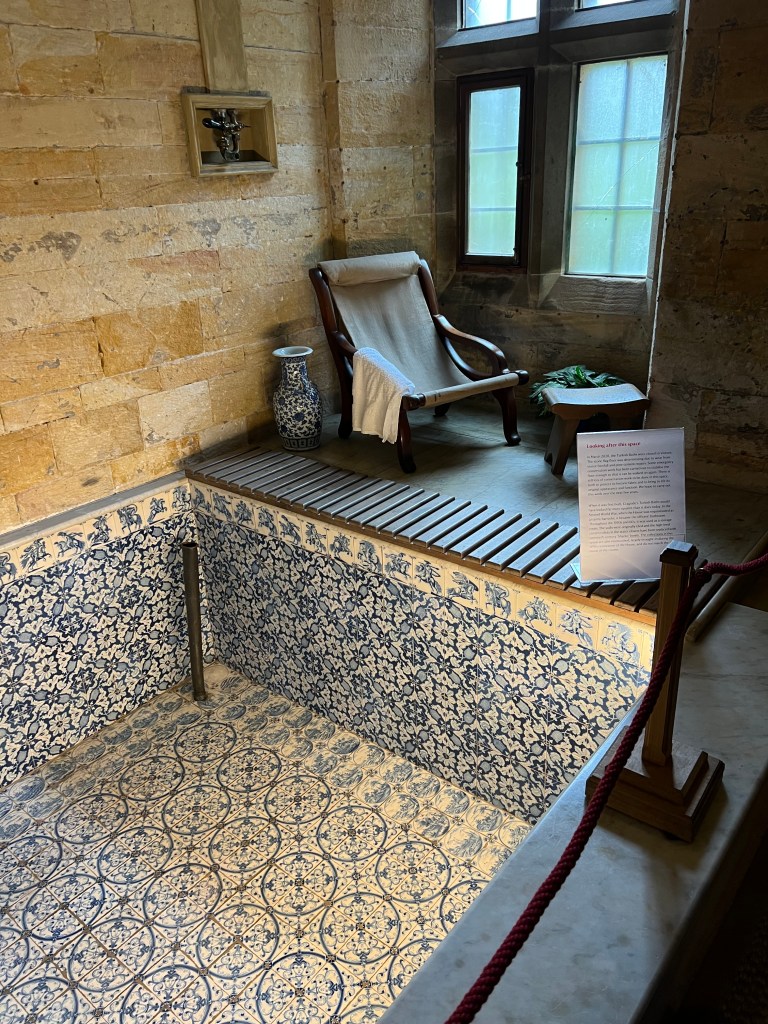 The empty plunge pool with blue and white floral tiles, next to the pool is a chair in front of a stone window. 