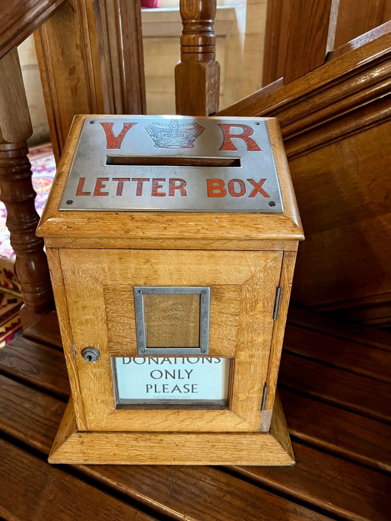 A small wooden postbox with the wording VR Letter box on a silver panel on the top and a sign saying donations only please. 