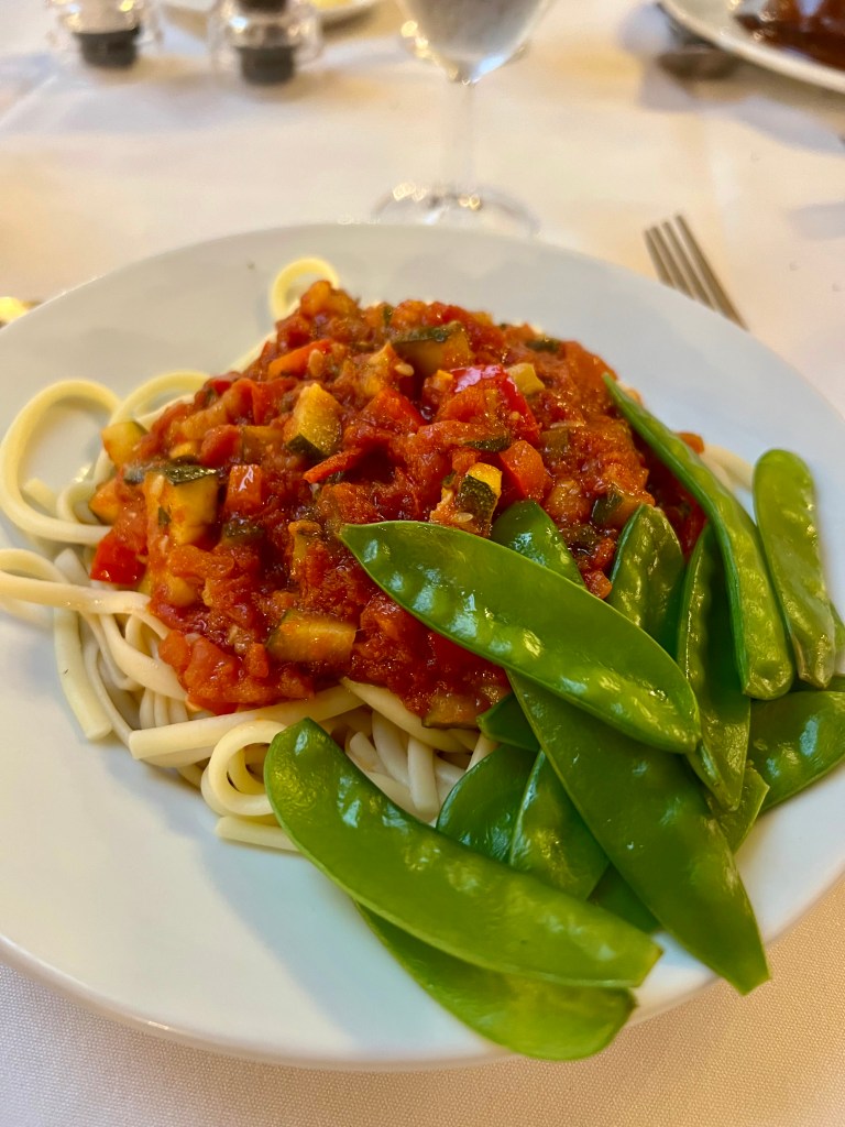 A bowl of spaghetti with a tomato and vegetable sauce and topped with mange tout.