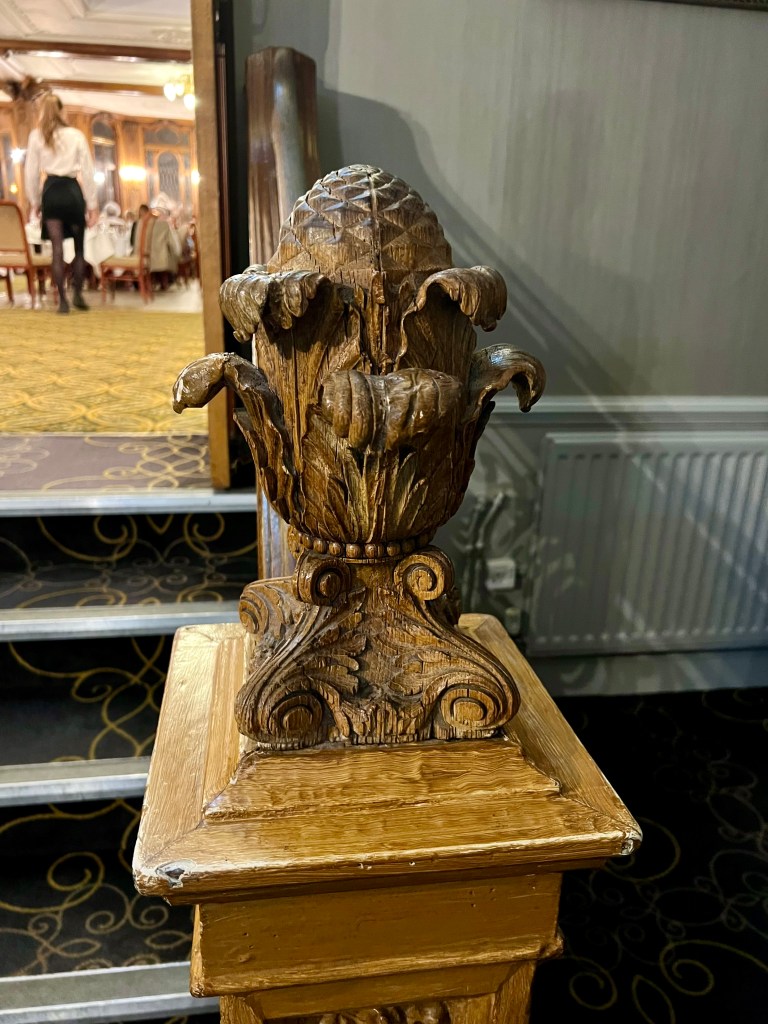 The bannister carving of an acorn with leaves around in the the stairs leading up to the Olympic dining room.