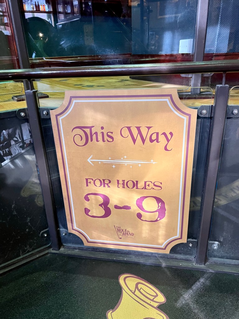 The photo shows a large yellow sign, written in red writing is 'This way for holes 3-9' aND A WHITE ARROW POINTING LEFT. 