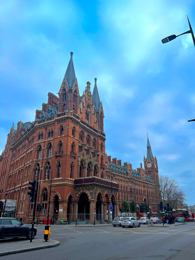 The photo shows the left most tower of the St Pancras hotel and St Pancras station building in red stone with gothic arched windows and turrets. The rod is seen in from of the building.