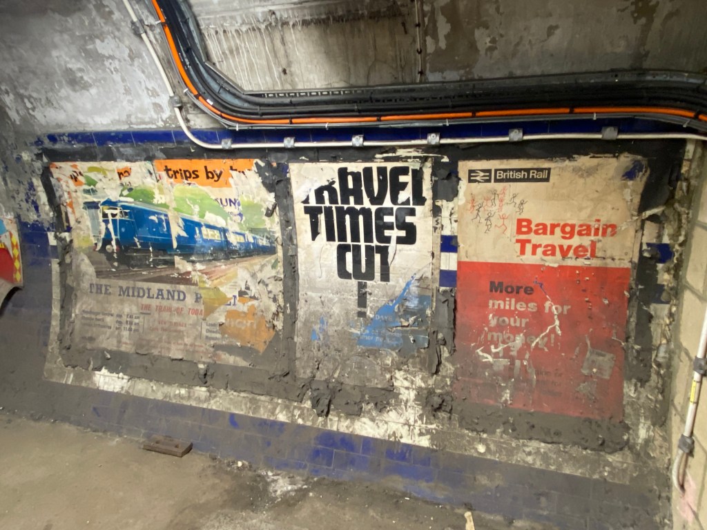 Three dirty and damaged posters on the wall of the tunnel.