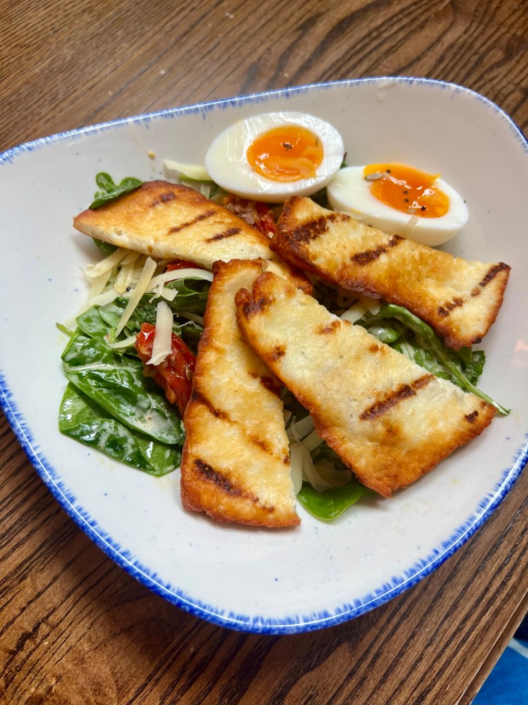A salad with a halloumi and a hard boiled egg. 