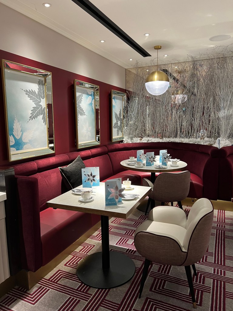 The seating area. there is red banquette seating with a small square and a small round table. Each table also has a white armchair and is set for afternoon tea with a white tease and blue and silver menus.