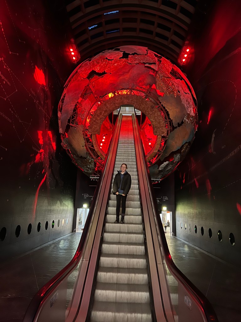 An escalator leading up through a giant meteorite that is glowing red. Am 11 year old girl