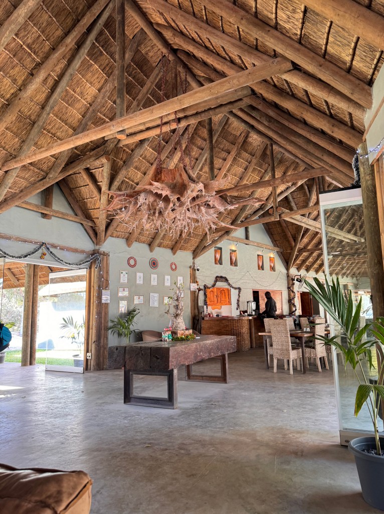 The reception area of Fathala with high beamed, thatched ceilings, the root of a large tree hanging from the ceiling and a large table. 