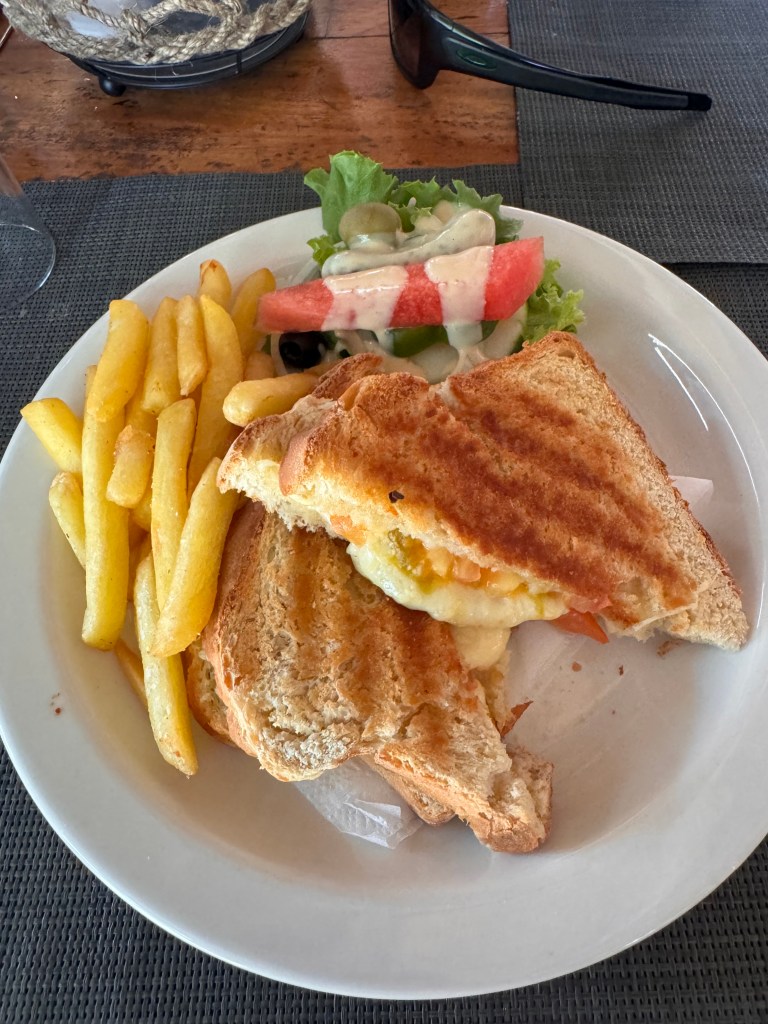 A cheese and tomato toast with chips and a side salad on a white plate. 