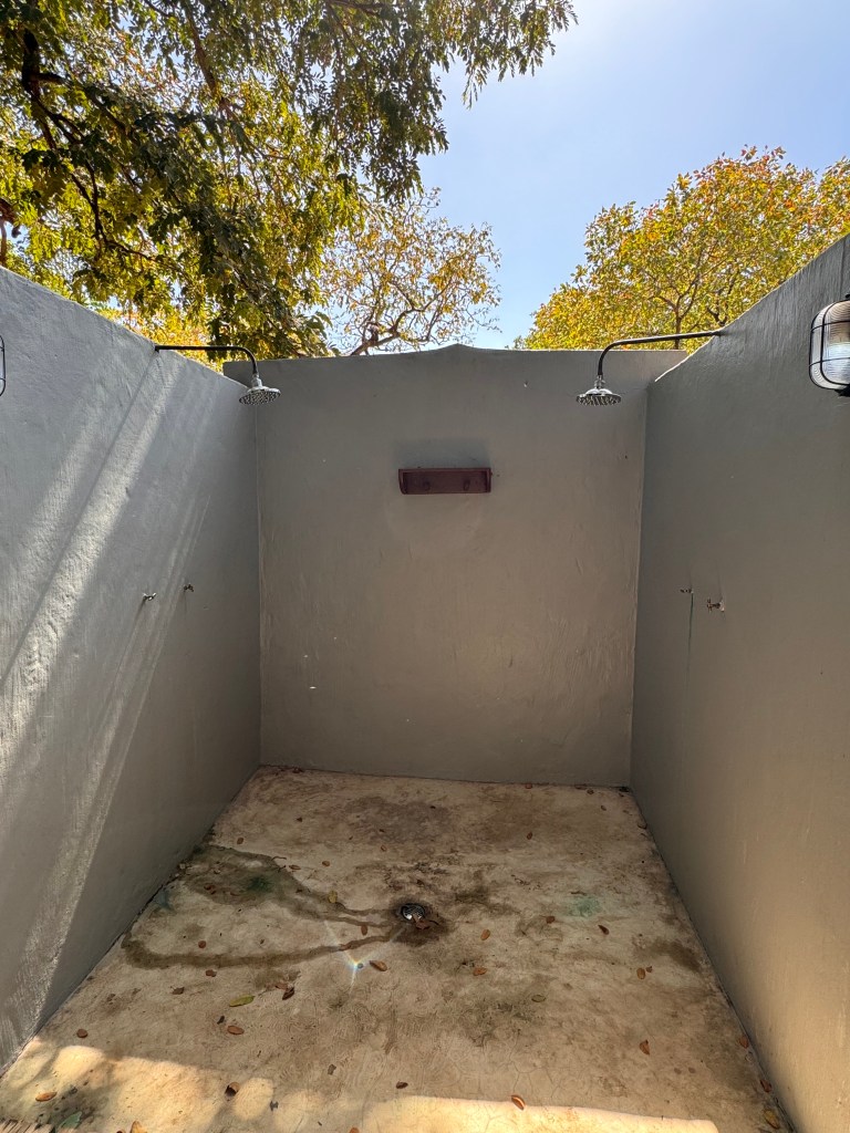 The outdoor shower. Three concrete walls with a shower head on each side and a drain in the middle. 