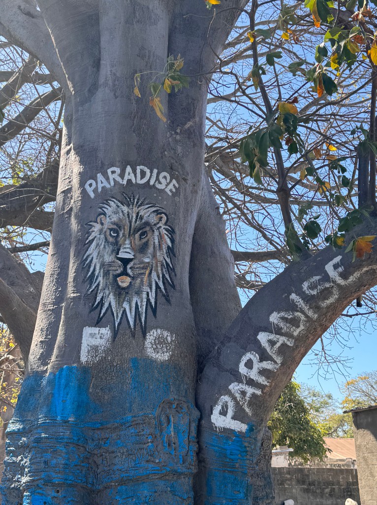 A large tree trunk painted with the face of a lion and the words Paradise. 