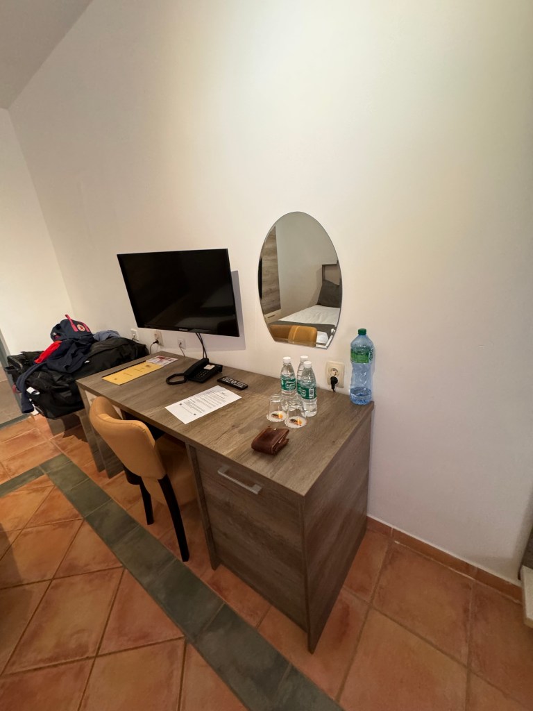 The desk area in the bedroom with a yellow chair, small mirror on the wall and a wall mounted TV. 