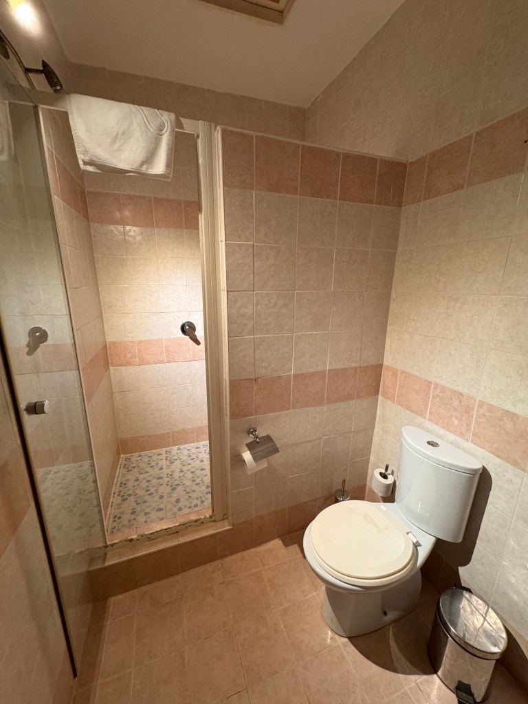 the bathroom which is decorated with peach and cream tiles showing the toilet on the right and the glass door to the walk in shower cubicle on the left. 