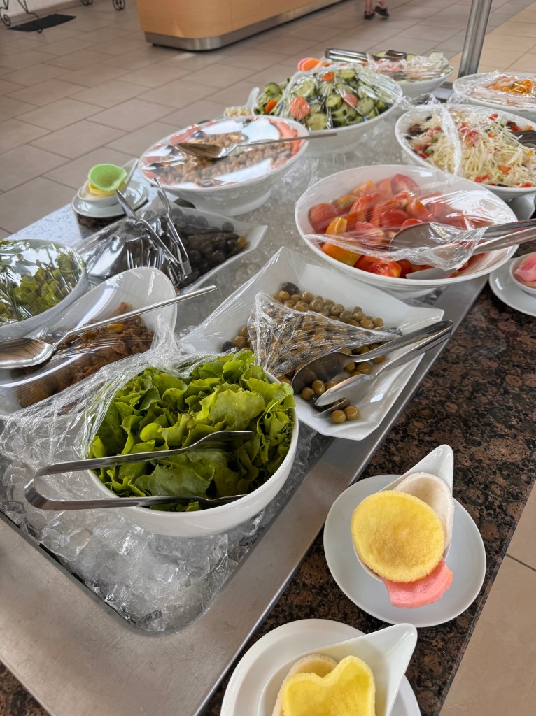 The salad bar with dishes of various salad items in large white bowls sitting on a bed of ice. 