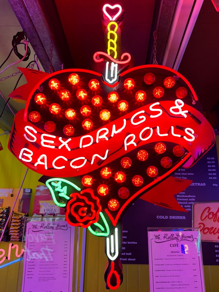 A neon sign that reads 'Sex, Drugs and Bacon Rolls' in a heart with a danger and a rose. 